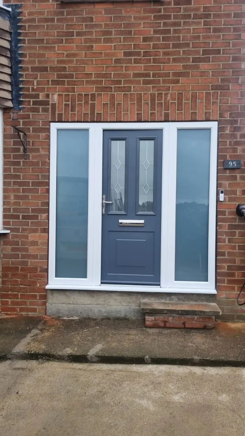 An anthracite composite door with two leaded glazed panels, flanked by two white-framed obscure-glazed sidelights, in red brick. A slate plaque reads 95.