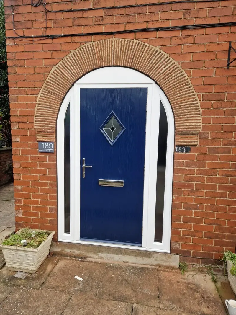 A royal-blue composite door with a diamond leaded panel and two arched glazed sidelights, set within a decorative radiating brick arch. A plaque reads 189 Cross Flatts Grove.