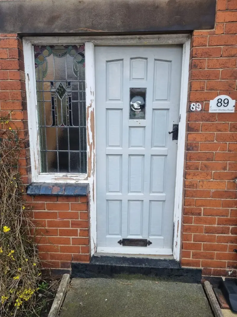 An old grey timber door with a peeling stained-glass side window, house number 89 on the plate.